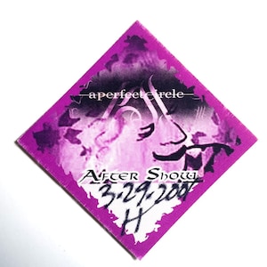 May include: A diamond-shaped ticket stub with a purple and black design. The ticket has the text "a perfect circle" at the top and "After Show 3.29.2004 H" at the bottom. The background is white.