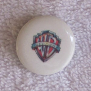 May include: White round button with a colorful Warner Bros. logo featuring the text "Warner Bros."