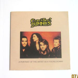 May include: A square, light brown album cover featuring the band Crash Test Dummies. The band members are in a portrait. The text "Crash Test Dummies" is in yellow and green. The text "A Portrait of the Artist as a Young Dummy" is below the portrait.
