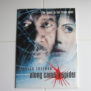 May include: Movie poster for the film "Along Came a Spider" starring Morgan Freeman. The poster features a close-up of Freeman's face and a woman's face, both partially obscured by a web-like pattern. The text "The game is far from over." is at the top of the poster.