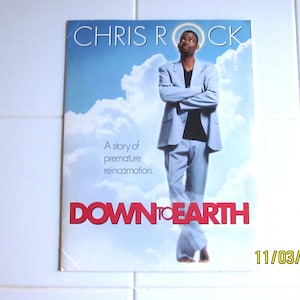 May include: A movie poster for "Down to Earth" featuring Chris Rock in a light blue suit against a sky background. The title is in red letters. The poster also includes the text "A story of premature reincarnation."