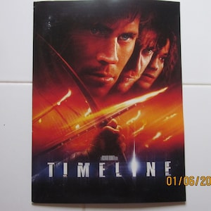 May include: A movie poster for the film "Timeline" featuring three people in a fiery, futuristic setting. The poster has a dark blue background with the title "TIMELINE" in white letters.
