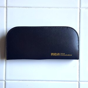 May include: A black leather case with gold lettering that reads "RCA Global Communications".