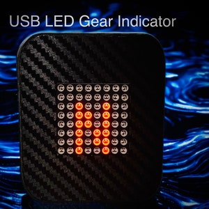 May include: A black USB LED gear indicator with a red LED display showing the number "1". The indicator has a carbon fiber pattern.