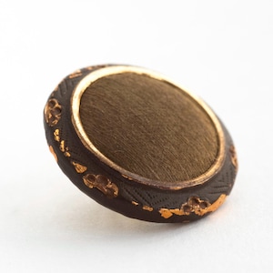 May include: A brown button with a gold-colored rim and a dark brown outer edge. The edge features a repeating pattern with gold accents. The center of the button is a lighter brown color.