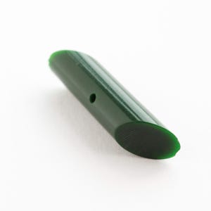 May include: A cylindrical dark green bead with a smooth, polished finish and a single small hole drilled through the center. The bead features slanted, oval-shaped ends, creating a sleek, elongated form with a consistent deep forest green color.
