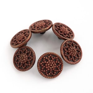 May include: Set of six antique copper-colored buttons. Each button has a raised, textured design with a central floral pattern surrounded by a beaded border. The buttons are arranged in a circular pattern against a white background.