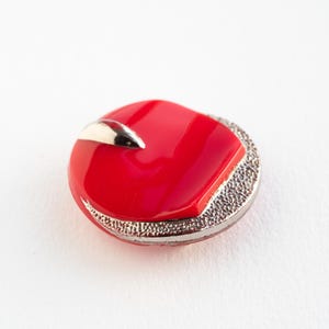 May include: A round, red button with a silver accent. The button has a textured silver border and a glossy red centre with a silver accent. Suitable for sewing projects and crafts.