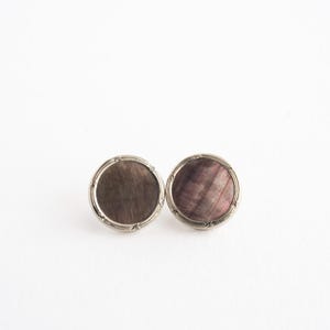 May include: A pair of round cufflinks with a silver-coloured border. Each cufflink features a dark, iridescent, textured centre with hints of purple and brown. The cufflinks are set against a white background.