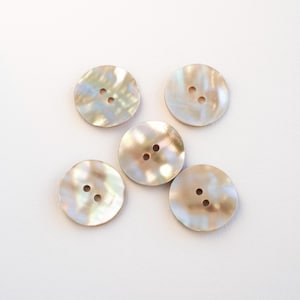 May include: Five round, iridescent buttons with two holes each, arranged in a star-like pattern. The buttons have a pearlescent sheen with hints of gold, white, and blue. These buttons are ideal for sewing and craft projects.