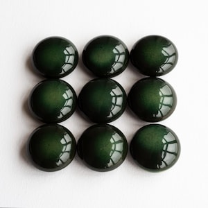 May include: Nine dark green, glossy, round cabochons arranged in a grid pattern. The cabochons have a smooth, polished surface with reflections. The color is a deep, rich green, and the overall effect is elegant and refined. These could be used for jewelry making or other crafts.