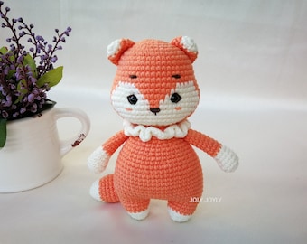 May include: A handmade orange and white crocheted fox doll with a white ruffled collar. The fox has white accents on its ears, paws, and tail. The doll is standing upright. The text "JOLY JOLY" is visible on the bottom right.