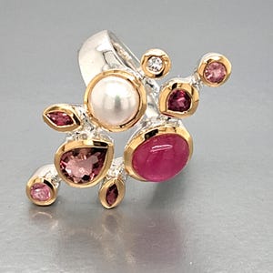 May include: A sterling silver ring with a cluster design. The ring features a large, round pearl, several pink gemstones, and a ruby-colored gemstone, all set in gold bezels. A small diamond is also set in the ring.