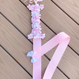 May include: A pink ribbon with a white bow attached to a pink and white flower letter I. The letter is made of foam and covered in fabric flowers.