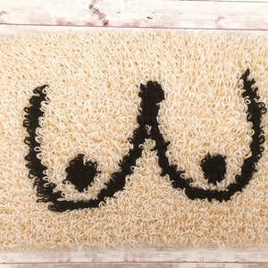 May include: A cream-colored bath mat with a black embroidered design of two breasts.