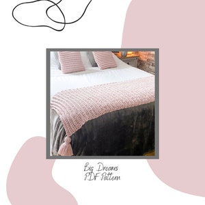 Puede incluir: Un cubrecama de crochet rosa con borlas sobre una cama con sábanas blancas y almohadas grises. El texto "Big Dreams PDF Pattern" está debajo de la imagen.