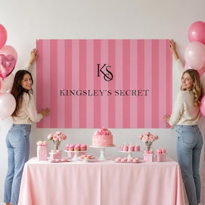 May include: A rectangular pink and light pink striped backdrop featuring the black text KINGSLEY'S SECRET and a logo with the letters KS. The backdrop is displayed above a table covered with a pink tablecloth, decorated with a cake and cupcakes.