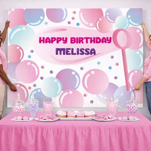 May include: A rectangular birthday backdrop featuring a white background with pink, purple, and blue bubble illustrations and a bubble wand. The text reads HAPPY BIRTHDAY MELISSA in pink and purple. The backdrop is displayed above a pink table.