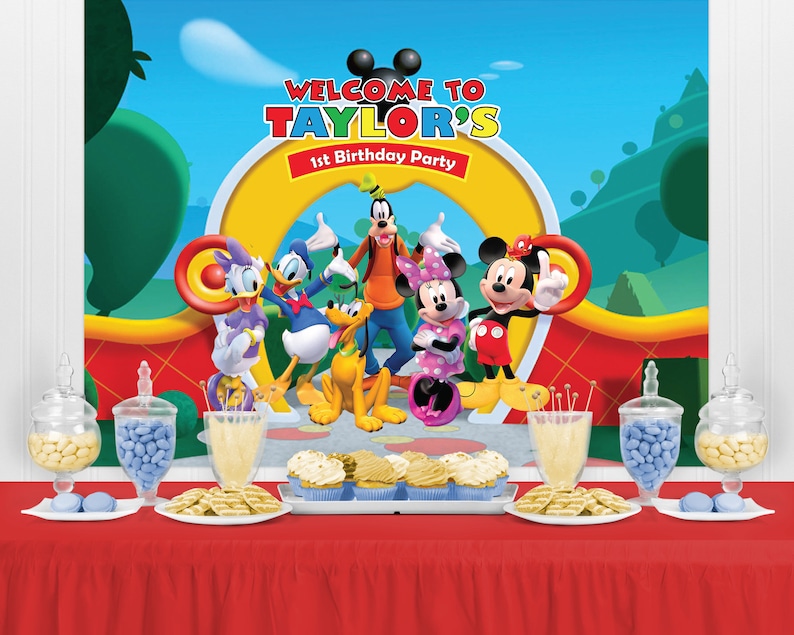 Puede incluir: Una colorida escena de fiesta de cumplea&ntilde;os con Mickey Mouse y sus amigos. El tel&oacute;n de fondo dice "Bienvenida a la 1&ordf; fiesta de cumplea&ntilde;os de Taylor". La mesa est&aacute; puesta con golosinas, incluyendo cupcakes, galletas y caramelos, con un mantel rojo.