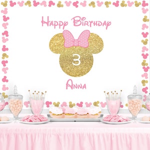 Peut inclure: D&eacute;coration de f&ecirc;te d'anniversaire sur le th&egrave;me de Minnie. La toile de fond blanche est orn&eacute;e de silhouettes de Minnie Mouse roses et dor&eacute;es. Elle pr&eacute;sente une t&ecirc;te de Minnie paillet&eacute;e dor&eacute;e avec un n&oelig;ud rose, le chiffre 3 et le nom "Anna".