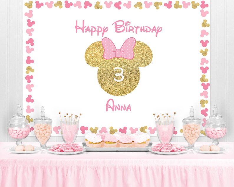 Peut inclure: D&eacute;coration de f&ecirc;te d'anniversaire sur le th&egrave;me de Minnie. La toile de fond blanche est orn&eacute;e de silhouettes de Minnie Mouse roses et dor&eacute;es. Elle pr&eacute;sente une t&ecirc;te de Minnie paillet&eacute;e dor&eacute;e avec un n&oelig;ud rose, le chiffre 3 et le nom "Anna".