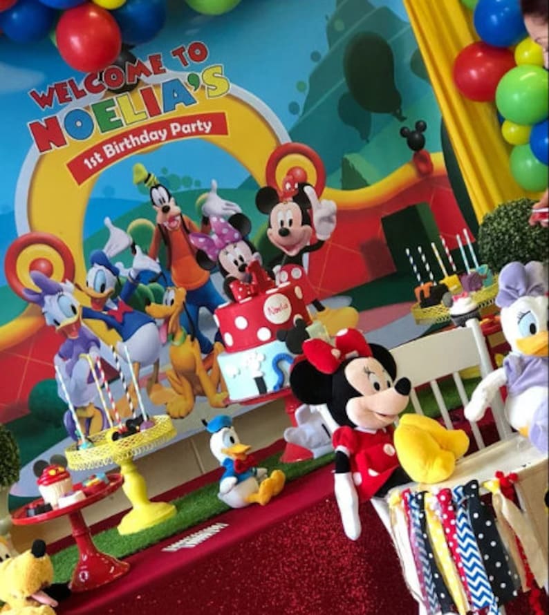 Puede incluir: Una escena de fiesta de cumplea&ntilde;os con Mickey Mouse y sus amigos. Una tarta con lunares rojos y un letrero que dice "Noelia's 1st Birthday Party" es el centro. Globos y decoraciones en rojo, amarillo y azul completan el ambiente alegre.
