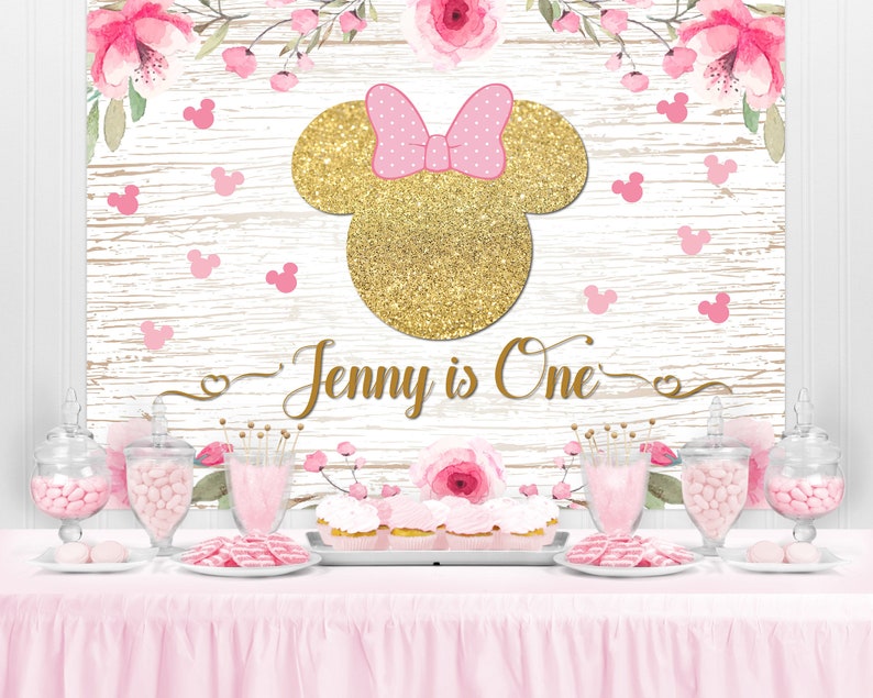 May include: A pink and gold Minnie Mouse themed backdrop with a wooden plank background. The backdrop has pink flowers, gold glitter, and the text "Jenny is One".