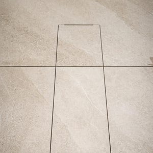 Könnte beinhalten: Nahaufnahme einer hellbeigen Steinoberfläche mit einem rechteckigen, eingelassenen Abdeckungsrahmen. Der Abdeckungsrahmen ist schwarz umrandet und bildet einen Kontrast. Der Stein weist subtile Maserungen auf.