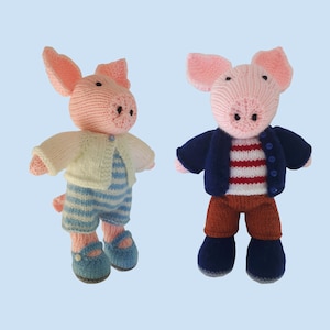 以下が含まれることがあります： 異なる服装をしたニットの豚のぬいぐるみ2体。1匹は白いカーディガンを着て、青と白のストライプのオーバーオールを履いています。もう1匹は紺色のジャケットを着て、赤と白のストライプのシャツと茶色のズボンを履いています。