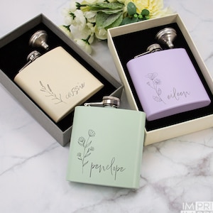 May include: Three personalized stainless steel hip flasks with floral designs and names "Cassie", "Eileen", and "Penelope". Each flask comes in a gift box with a funnel.