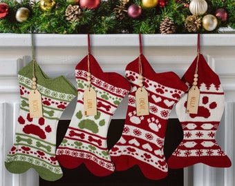 May include: Four personalized dog bone-shaped Christmas stockings with red and green knit patterns and wooden tags with the names "Boots", "Luna", "Chewie", and "Bella".