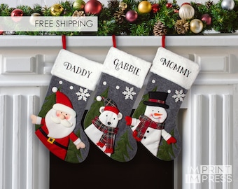 May include: Three gray Christmas stockings with white fur trim, personalized with the names "Daddy", "Gabbie", and "Mommy". Each stocking features a different festive character: Santa Claus, a polar bear, and a snowman.