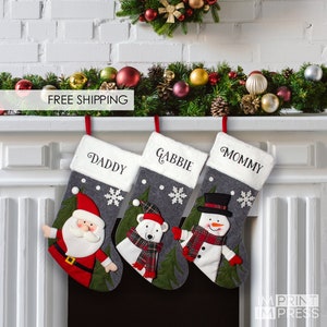May include: Three gray Christmas stockings with white fur trim, personalized with the names "Daddy", "Gabbie", and "Mommy". Each stocking features a different festive character: Santa Claus, a polar bear, and a snowman.