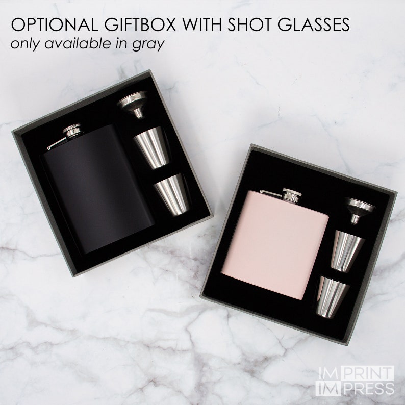 Puede incluir: Dos cajas de regalo con matraces de cadera negros y rosas y vasos de chupito. Las cajas est&aacute;n forradas con terciopelo negro. El texto de la imagen dice "OPTIONAL GIFTBOX WITH SHOT GLASSES only available in gray".