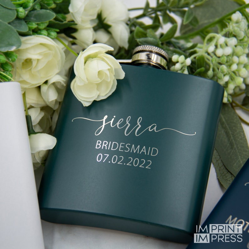Puede incluir: Una petaca de metal verde oscuro con una tapa plateada. La petaca est&aacute; grabada con el texto "sierra bridesmaid 07.02.2022" en una fuente plateada.
