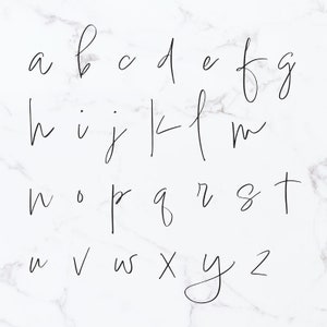 May include: A handwritten alphabet in black ink on a white marble background.