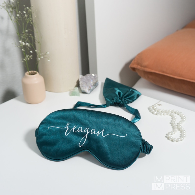 An emerald sleep eye mask shown with a matching carry pouch and with a name in white vinyl