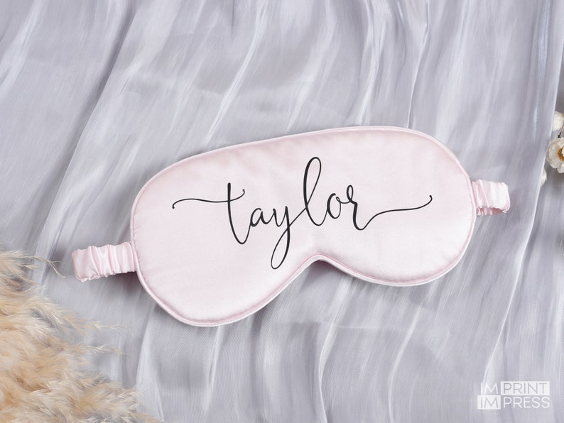May include: A pink satin sleep mask with the name "Taylor" written in black cursive script.