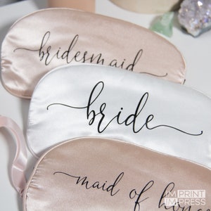 May include: Three satin sleep masks with the words "bridesmaid", "bride", and "maid of honor" printed in black script.