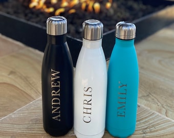 Op de afbeelding: Drie roestvrijstalen waterflessen met gepersonaliseerde namen: Andrew, Chris en Emily. De flessen zijn zwart, wit en turquoise.