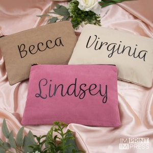 May include: Three personalized zippered pouches in beige, cream, and pink with black lettering. The pouches are labeled "Becca", "Virginia", and "Lindsey".