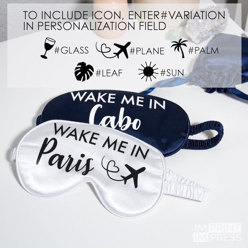 May include: Two satin sleep masks, one navy blue and one white. The navy blue mask says "Wake Me In Cabo" and the white mask says "Wake Me In Paris" with a plane icon.