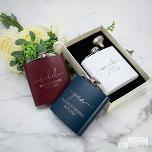 Puede incluir: Tres matraces de acero inoxidable personalizados con nombres y t&iacute;tulos grabados. Los matraces son de color rojo, blanco y azul. El texto en los matraces dice "Rachel Maid of Honor 07.02.2022", "Amanda Bride 07.02.2022" y "Jenn Mother of the Bride 07.02.2022".