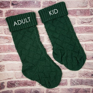 May include: Two green knitted Christmas stockings with white embroidered text. The larger stocking says "Adult" and the smaller stocking says "Kid".