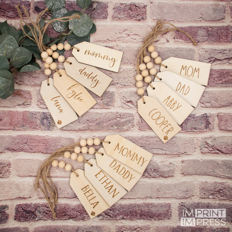 May include: Wooden gift tags with names like "Mommy", "Daddy", "Ethan", and "Bella" on them. The tags are strung together with wooden beads and twine. The tags have a paw print design.