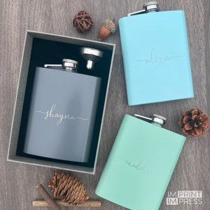 May include: Three personalized stainless steel hip flasks, one gray, one light blue, and one light green. The flasks are engraved with the names "Shayna", "Alexa", and "Madeline".