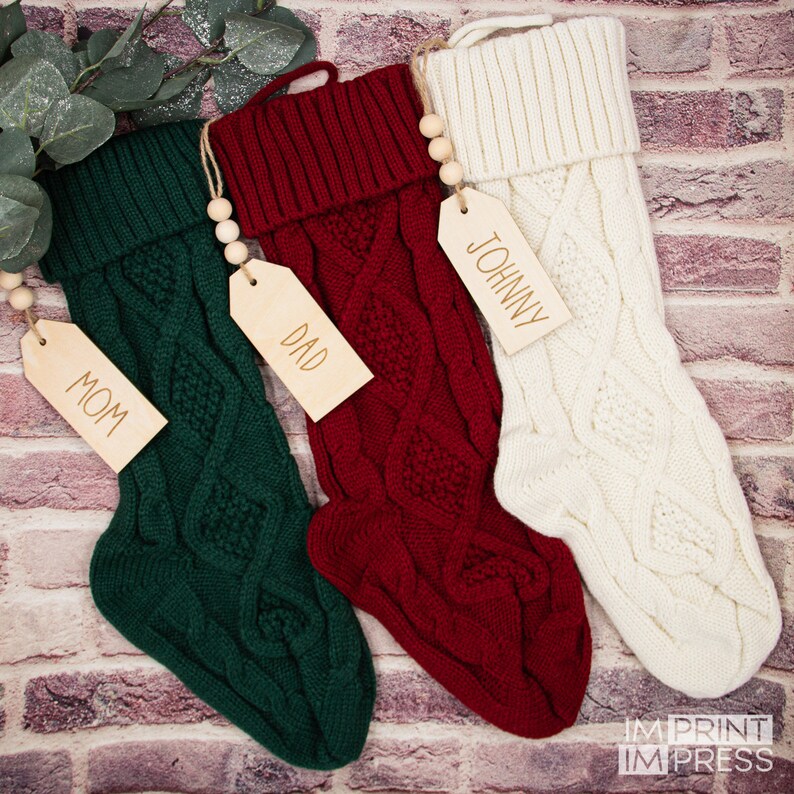 May include: Three knitted Christmas stockings in green, red and white with wooden tags that say "Mom", "Dad", and "Johnny".