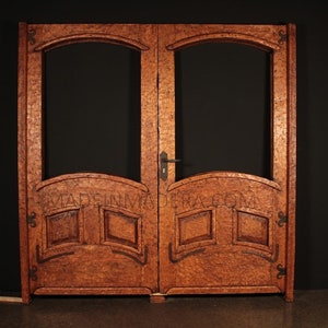 May include: A pair of double wooden doors with arched glass panels and intricate carvings. The doors are a rich brown colour and have a rustic, antique look.