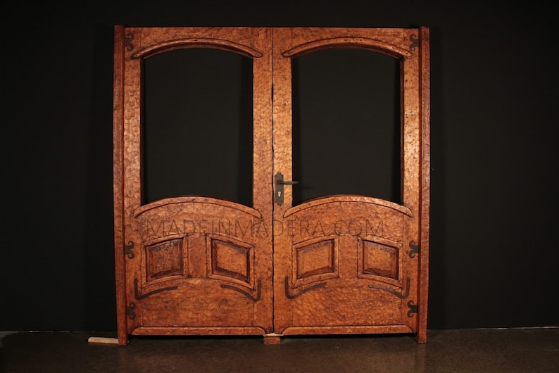 May include: A pair of double wooden doors with arched glass panels and intricate carvings. The doors are a rich brown colour and have a rustic, antique look.
