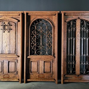 May include: Three wooden doors with intricate ironwork details. The doors are all different styles, with one featuring a simple square design, another with a more ornate scroll design, and the third with a double door design with vertical bars. The doors are all made of dark wood and have a rustic look.